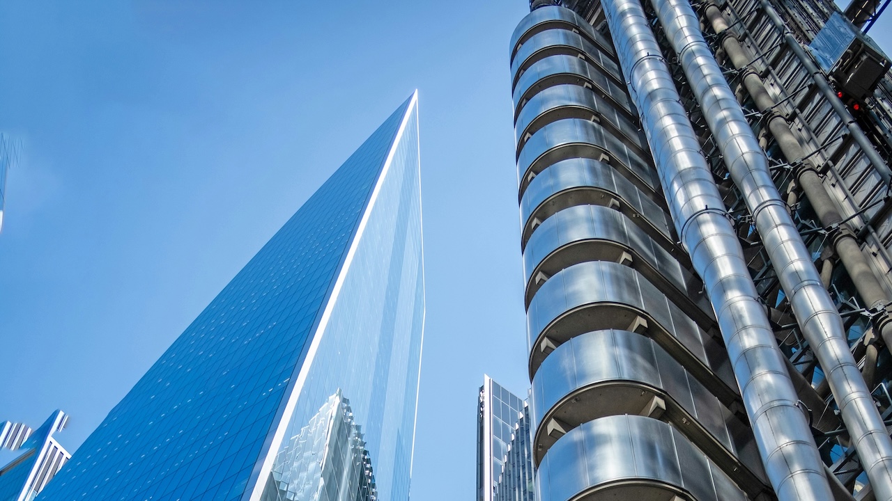 A view of the Lloyd's of London building looking up from ground level with a blue sky behind